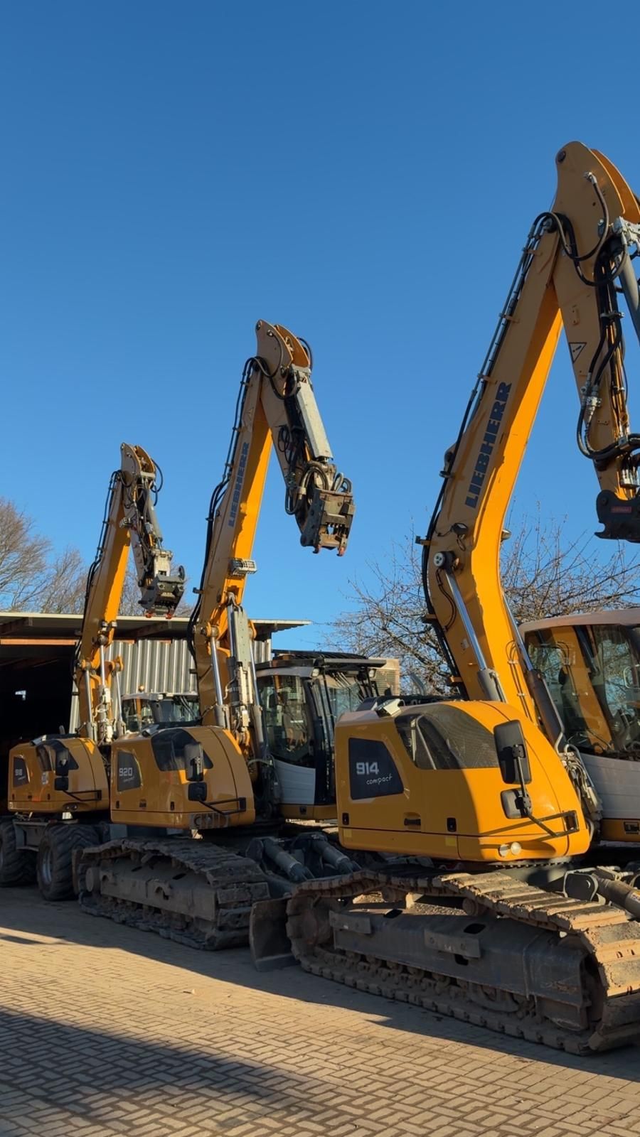 Drei gelbe Liebherr-Bagger von JD Senzel nebeneinander vor einer Halle