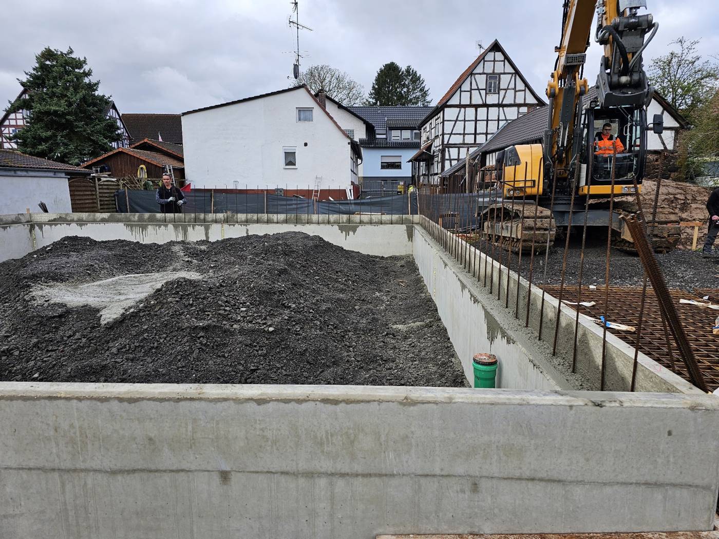 Baustelle von JD Senzel: Baugrube mit Betonwänden und Bagger zwischen Fachwerkhäusern