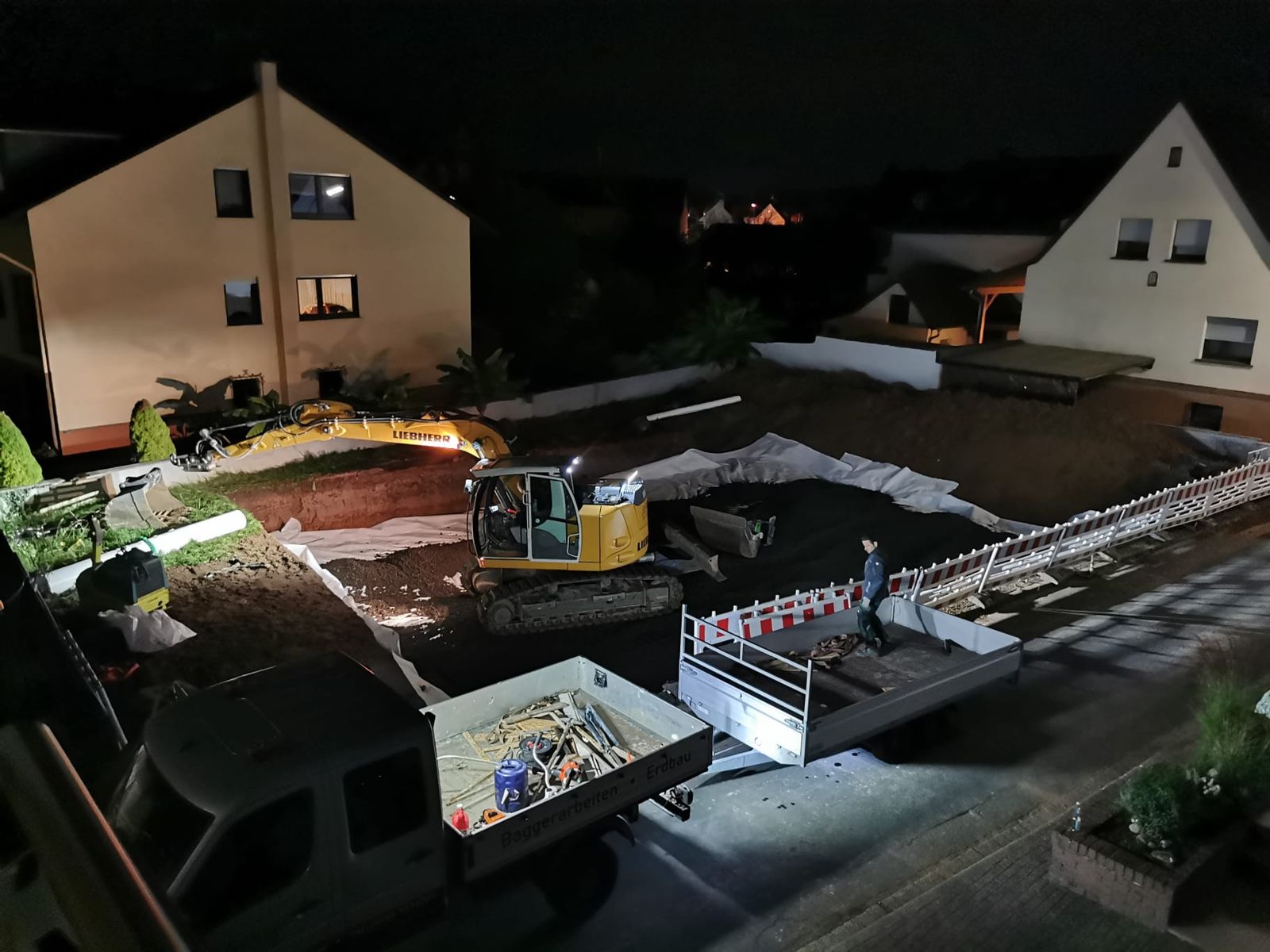 Nachtbaustelle mit Flutlicht: Liebherr-Bagger und Pritsche mit Aufschrift Baggerarbeiten Erdbau